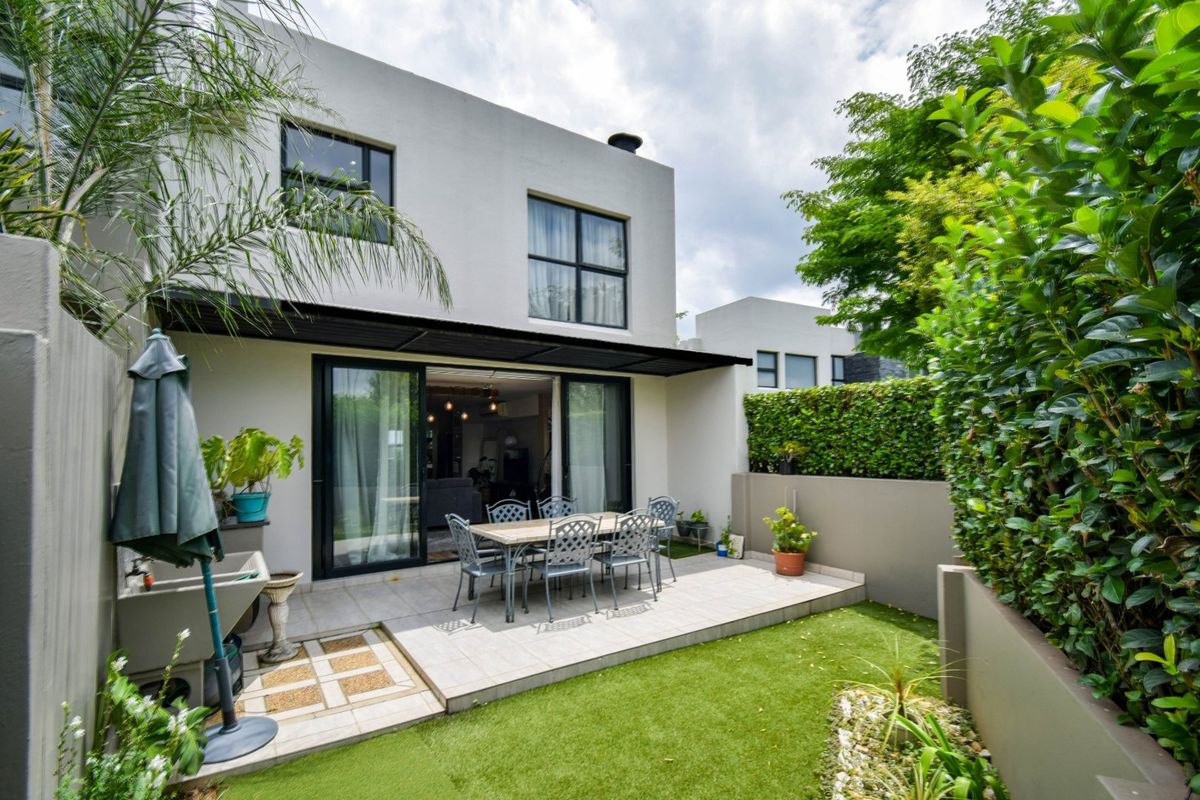 A well-maintained rear exterior featuring a tiled patio, artificial lawn, and sliding glass doors leading into the home.