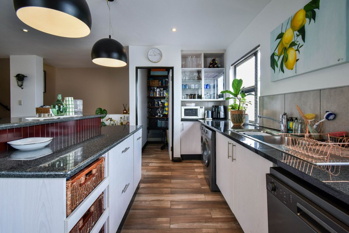 Modern kitchen featuring granite countertops, ample cabinetry, integrated appliances, and a convenient walk-in pantry, finished with contemporary lighting and wood-look flooring.