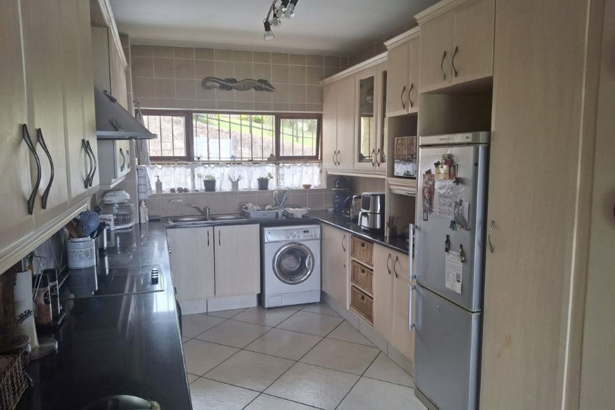 A functional kitchen featuring light-toned cabinetry, dark granite countertops, tiled flooring, and integrated laundry plumbing, offering a practical layout for daily use.