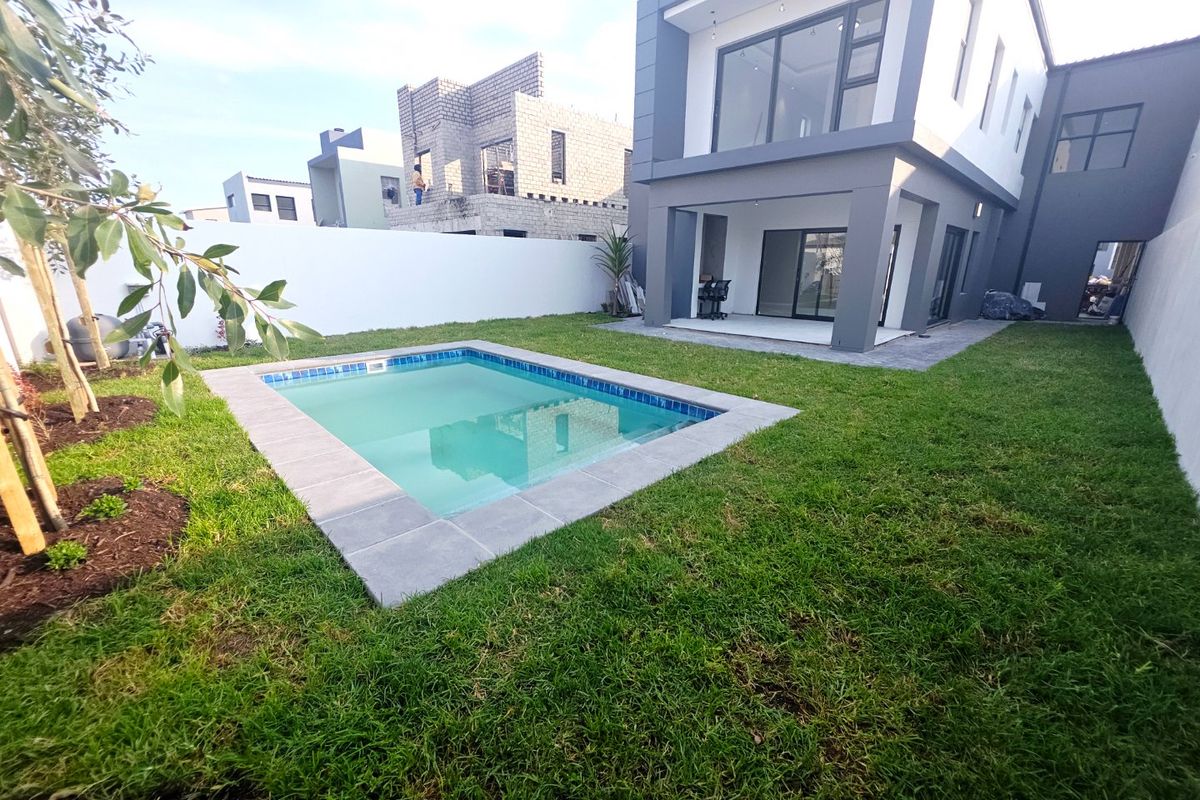 Rear view of a modern two-story house featuring a private swimming pool, landscaped lawn, and a covered patio area.
