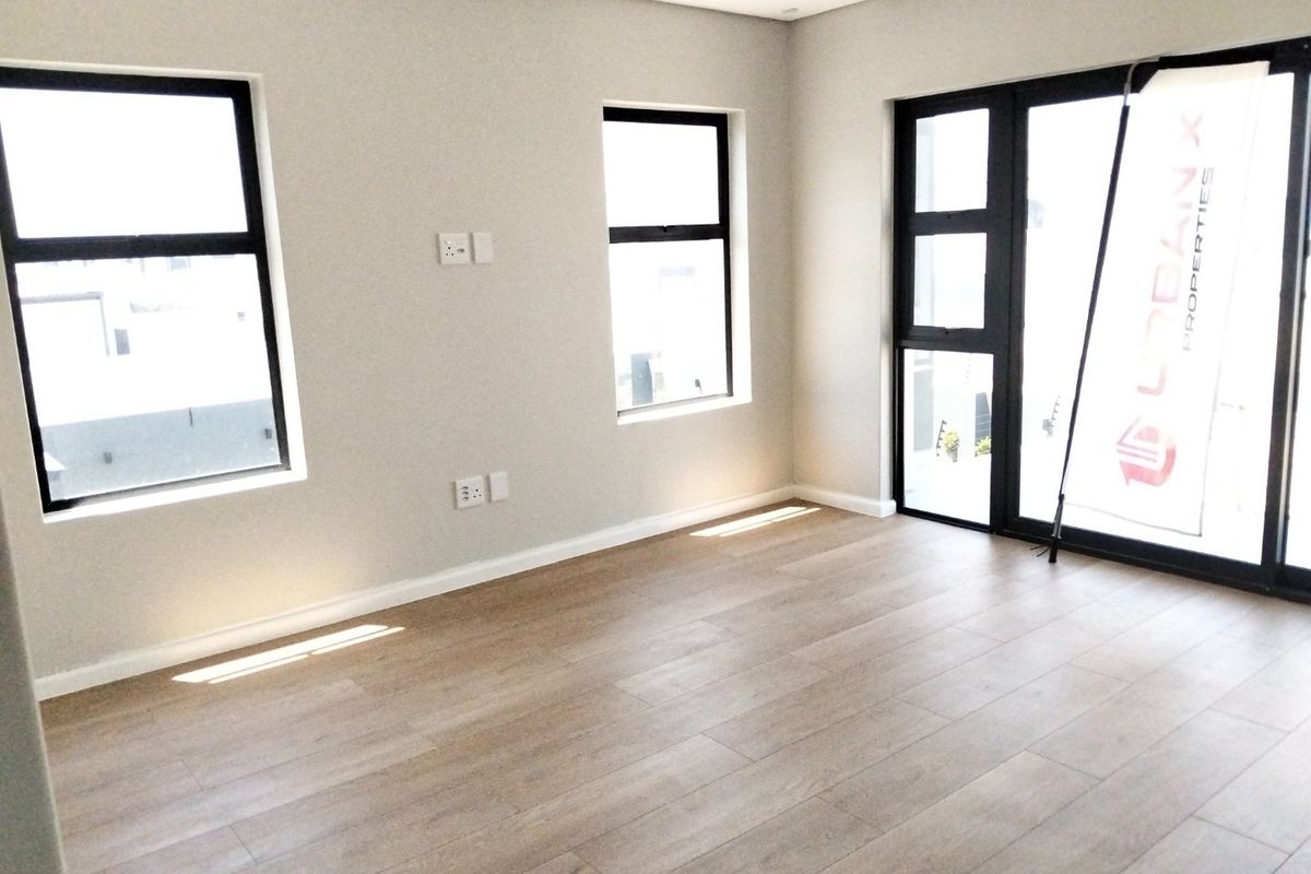 A bright, modern living area featuring light wood-look flooring, recessed ceiling lighting, and large black-framed windows and sliding doors.