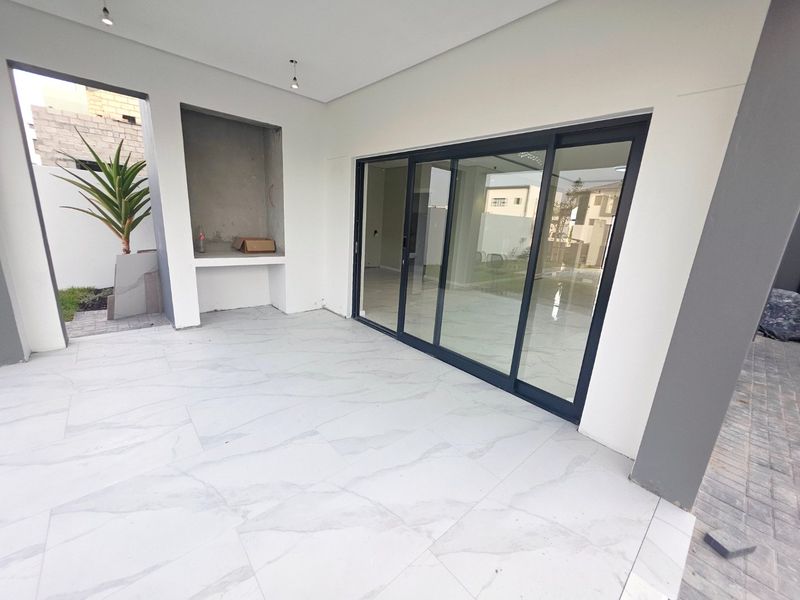 A modern covered patio area featuring large format marble-look floor tiles, a built-in barbecue niche, and expansive sliding glass doors leading to the interior.