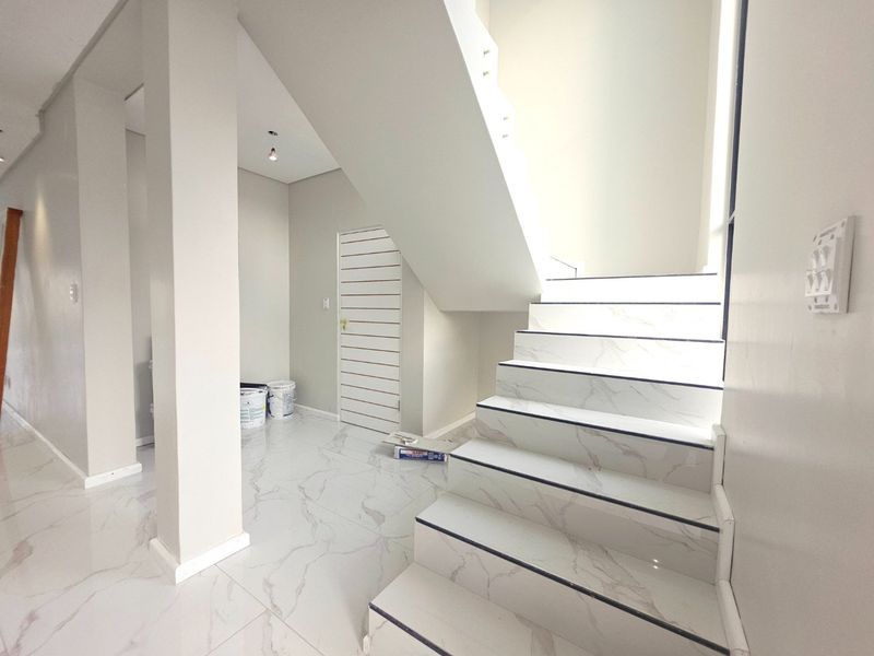 A bright, modern entrance hall featuring marble-look tiled flooring and a contemporary staircase with integrated lighting.