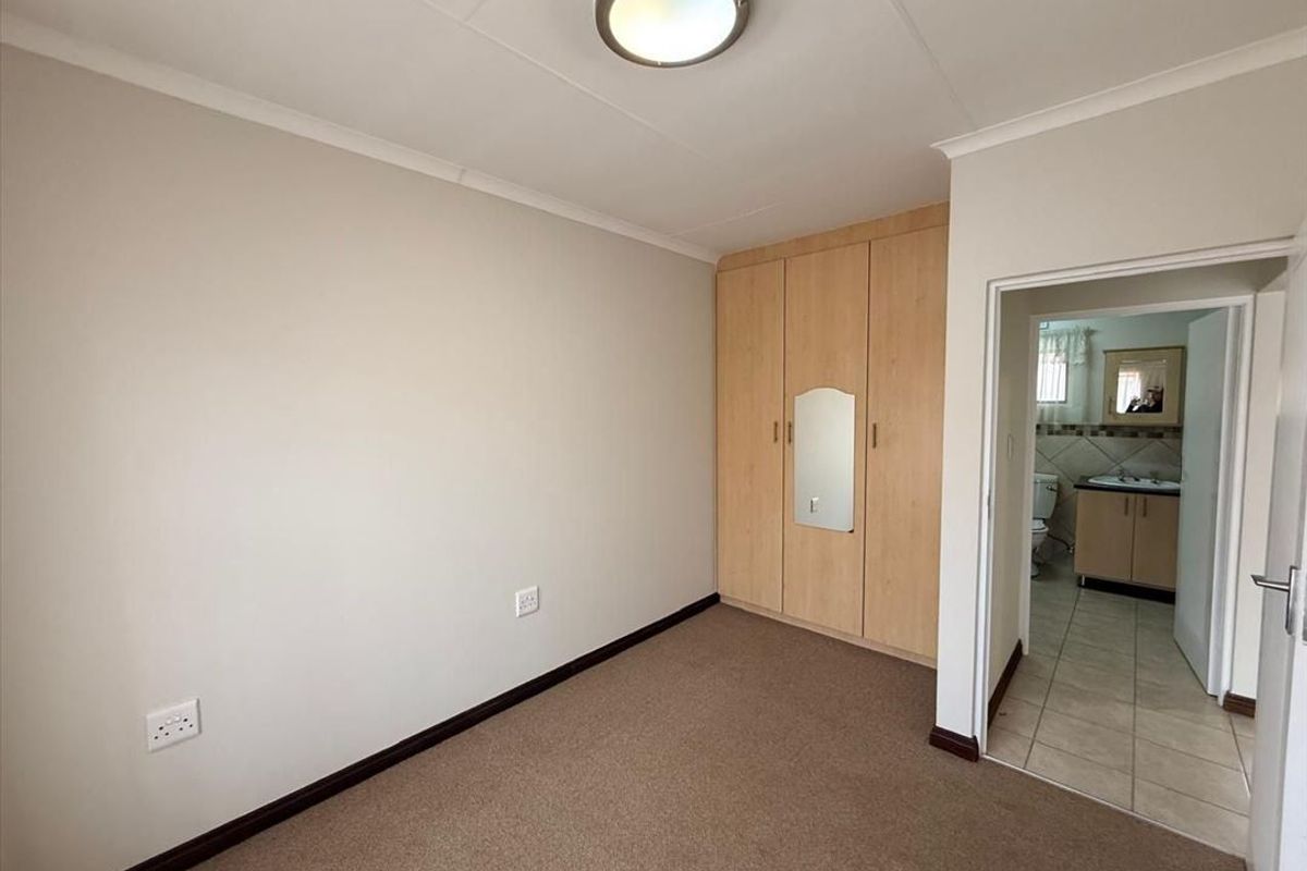 A clean, empty bedroom featuring built-in wooden cupboards, carpeted flooring, and direct access to an en-suite bathroom.