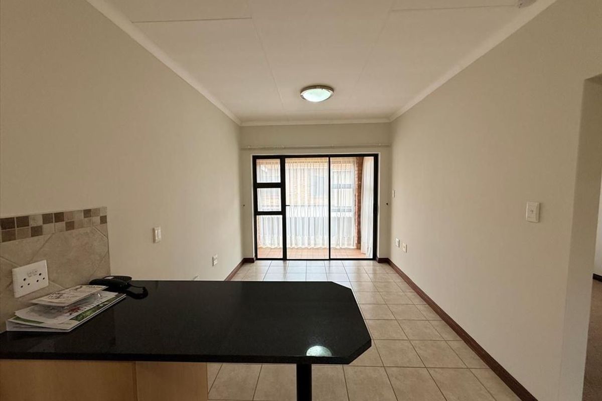 An open-plan living and kitchen area featuring tiled flooring, a granite breakfast bar, and sliding glass doors leading to an outdoor balcony.