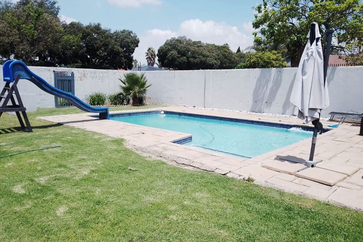 Outdoor pool area featuring a rectangular swimming pool with paved surround, perimeter wall, and lawn area.