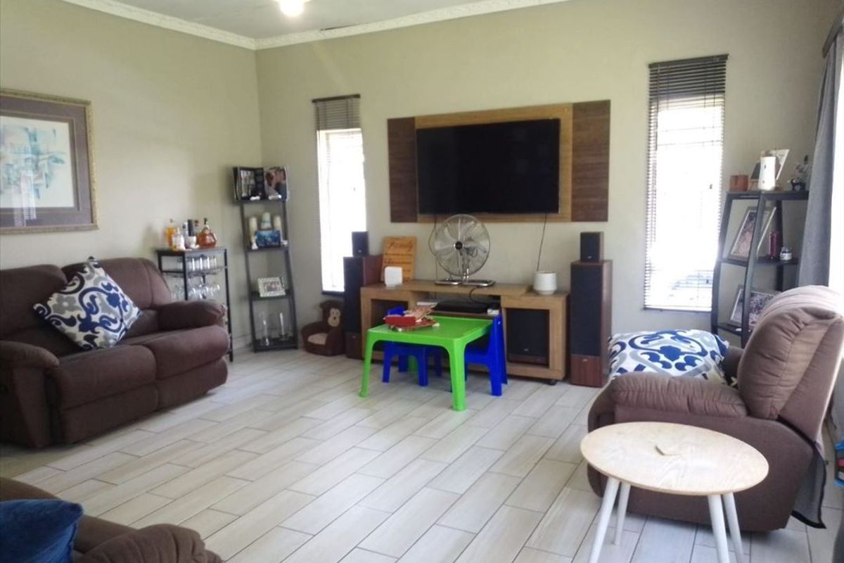 A comfortable living room featuring tiled flooring, a built-in media wall unit, and venetian blinds, providing a functional and well-lit family space.