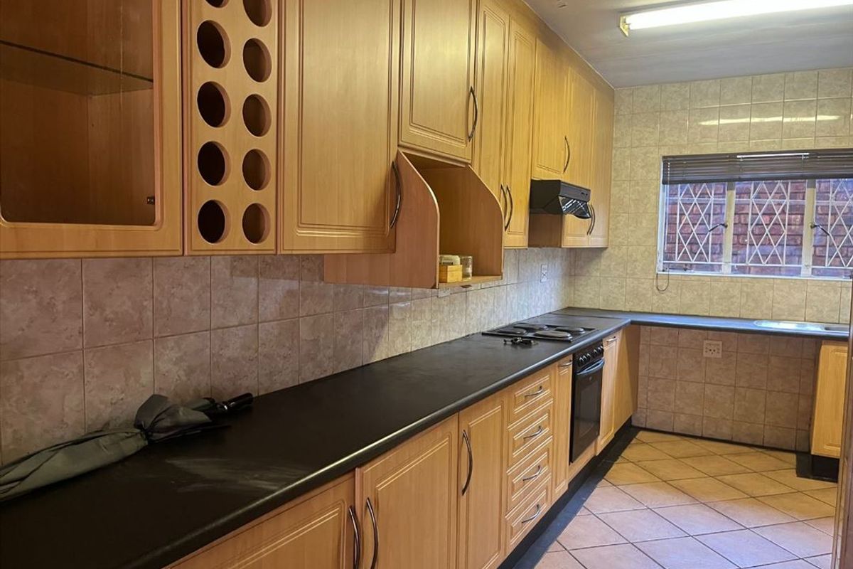 A functional kitchen featuring light wood cabinetry, dark laminate countertops, built-in oven and hob, and tiled flooring.
