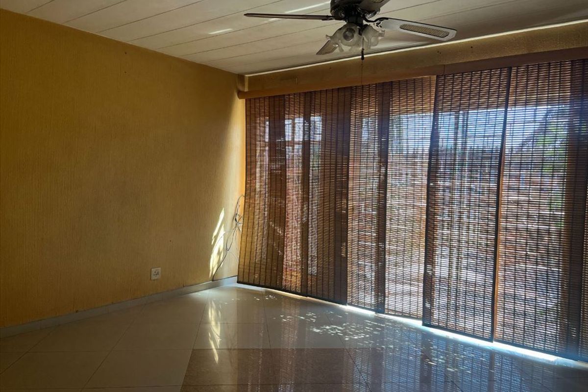 A spacious living area featuring tiled flooring, a ceiling fan, and large sliding glass doors with bamboo blinds leading to an outdoor space.