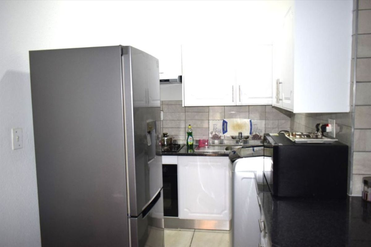 A compact kitchen featuring white cabinetry, dark granite countertops, tiled backsplash, and integrated cooking appliances.