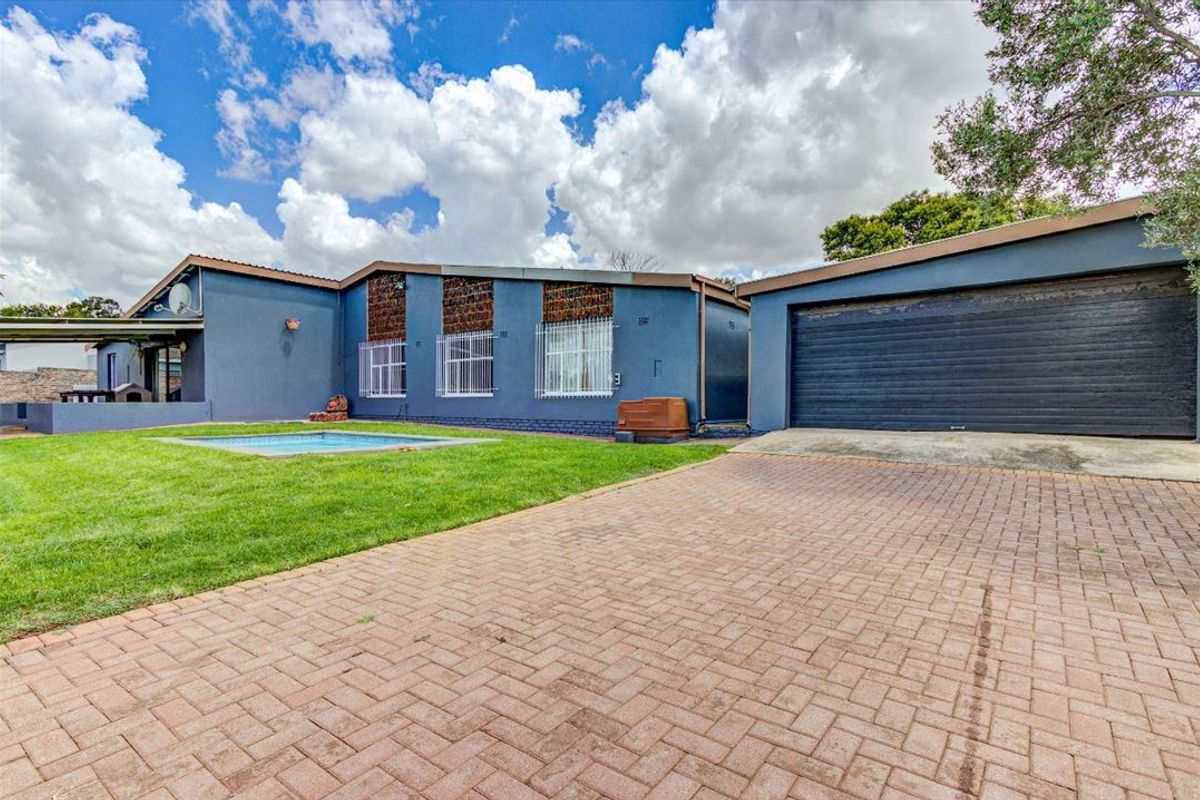 Rear exterior view featuring a paved driveway, attached garage, and a swimming pool set within a landscaped garden area.