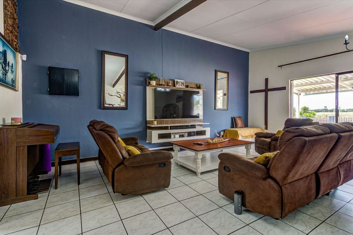 A spacious living room featuring tiled flooring, an exposed ceiling beam, and a built-in media console, with direct access to an outdoor area.