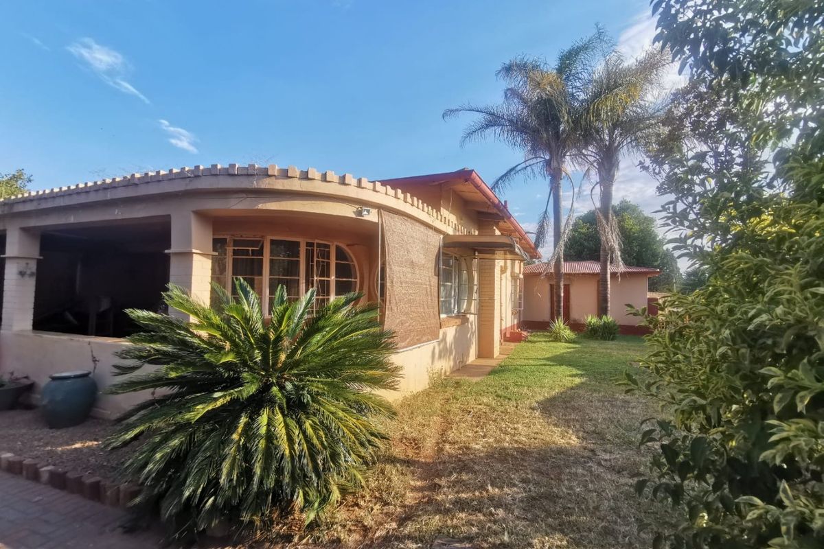 Rear view of the house featuring a covered patio area, established garden, and traditional brick construction with steel-framed windows.