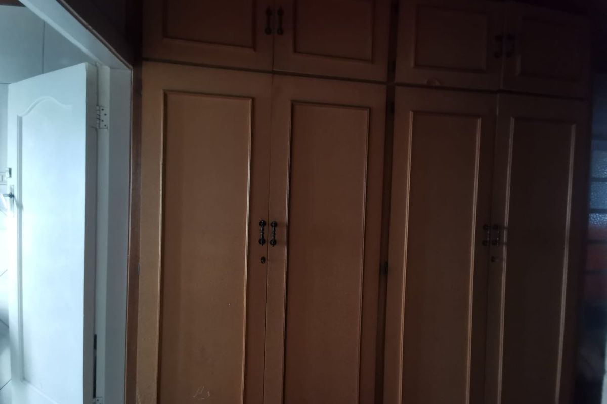 A bedroom featuring dated, full-height built-in wooden cupboards with overhead storage compartments.