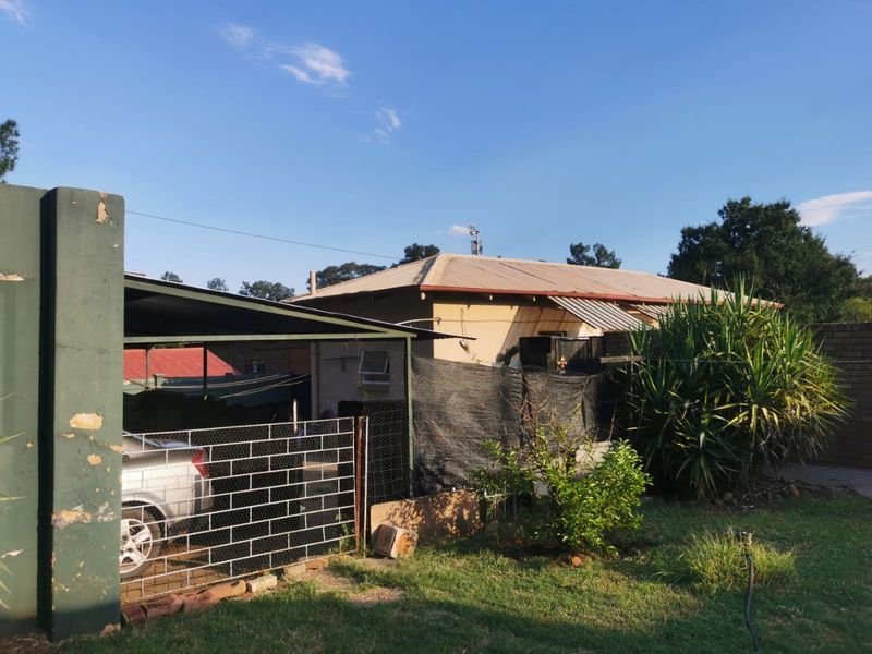 Rear view of the property featuring a carport, metal roofing, and established garden area with security fencing.