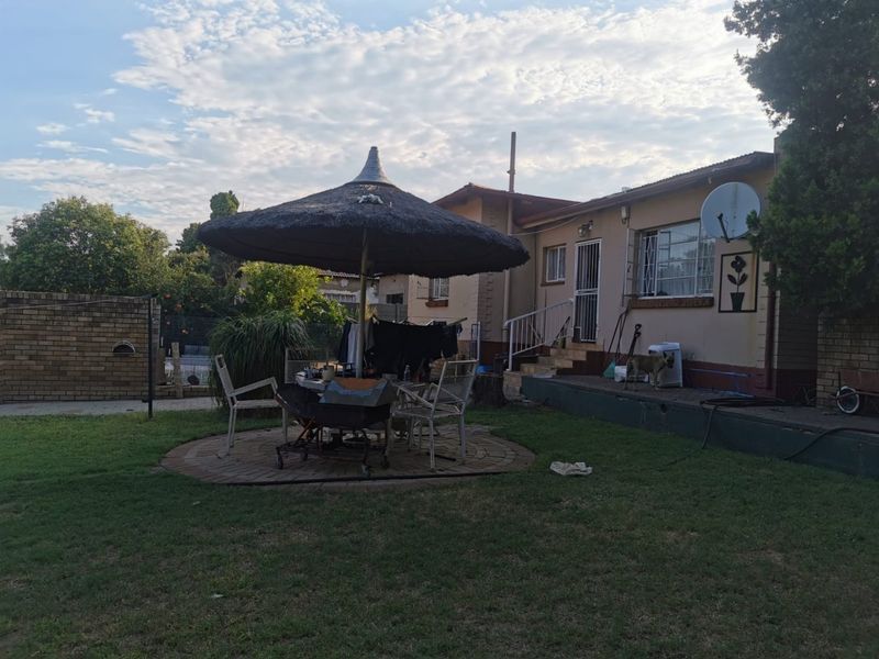 Rear view of the property featuring a paved patio area, lawn, and exterior building facade with security features.