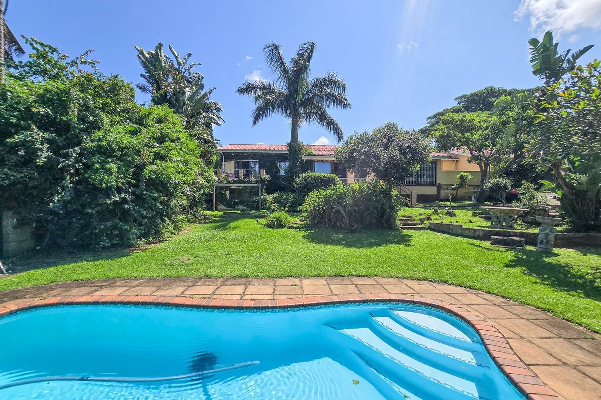 A spacious rear garden featuring a swimming pool with brick coping, lush landscaping, and a view of the house exterior with a tiled roof.