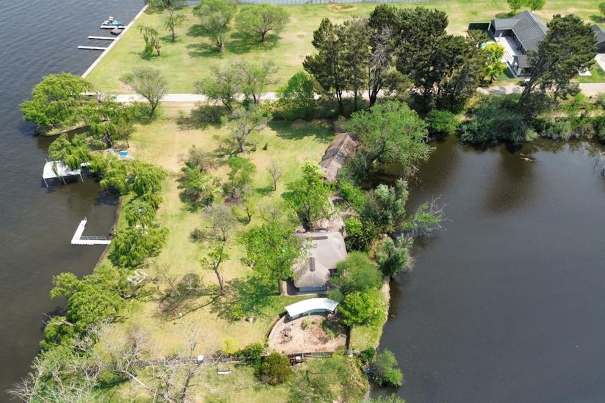 Aerial view of a sprawling waterfront farm property featuring expansive green lawns, mature trees, private jetty access, and multiple thatched-roof structures.