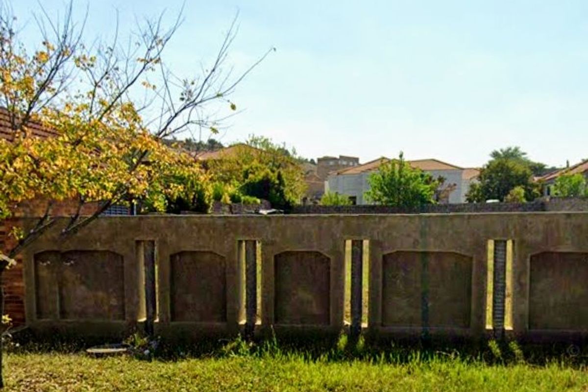 A view of a vacant residential plot featuring a weathered precast concrete boundary wall and street-side verge.