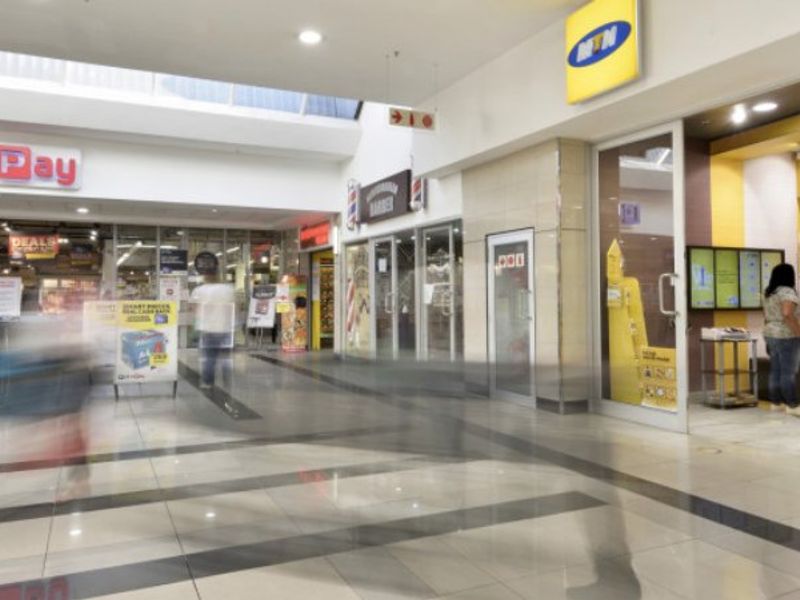 A well-maintained commercial shopping center hallway featuring polished tiled flooring, recessed lighting, and multiple glass-fronted retail storefronts.