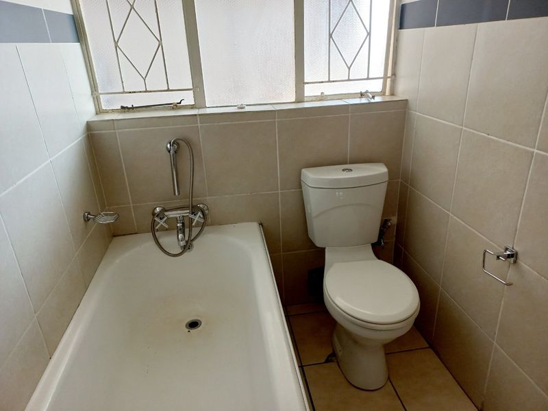 A functional bathroom featuring a bathtub, toilet, and neutral wall tiling. The space is ready for a modern update to enhance its appeal.
