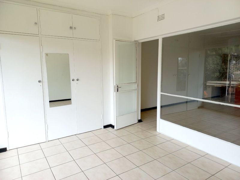 A bright, empty office space featuring tiled flooring, built-in storage cupboards, and a large glass partition wall providing natural light.
