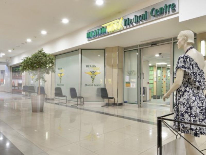 Commercial medical centre entrance featuring a glass storefront, automatic sliding doors, and polished tiled flooring within a shopping centre environment.