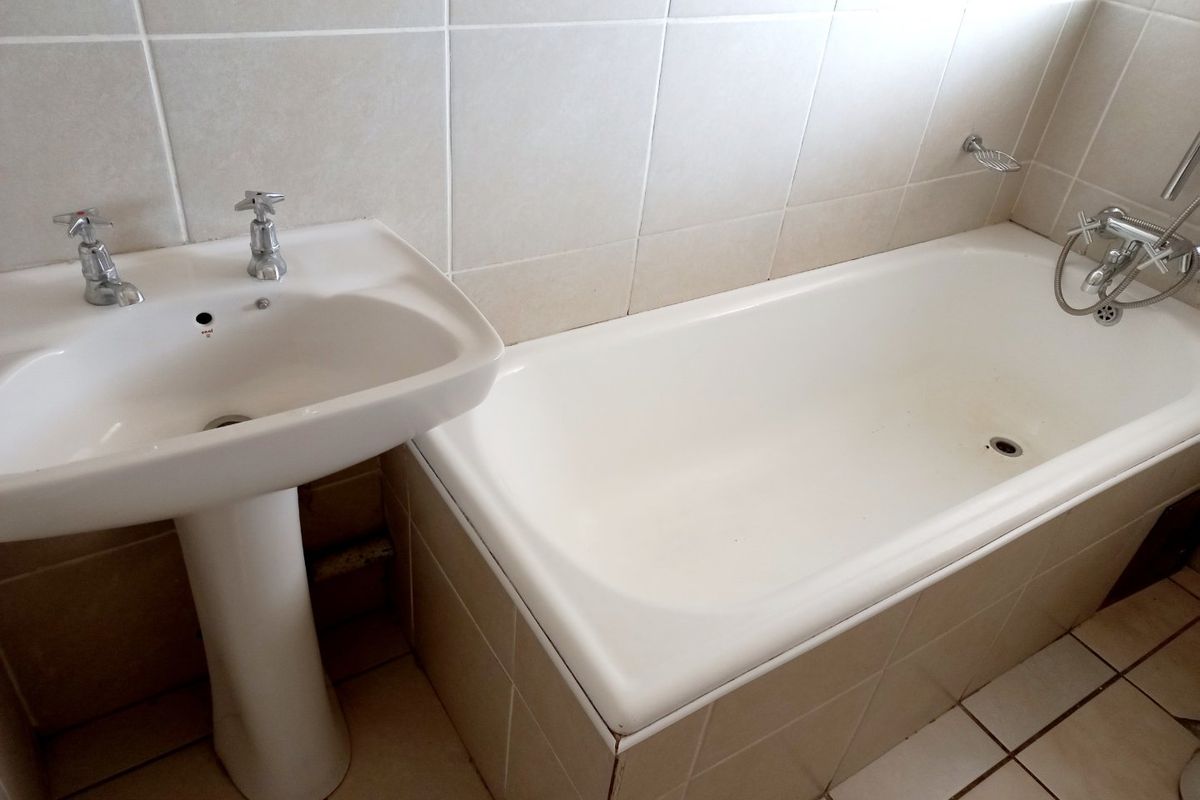 A functional bathroom featuring a pedestal basin and a built-in bathtub with tiled surrounds and flooring.