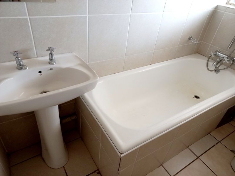A functional bathroom featuring a pedestal basin and a built-in bathtub with tiled surrounds and flooring.