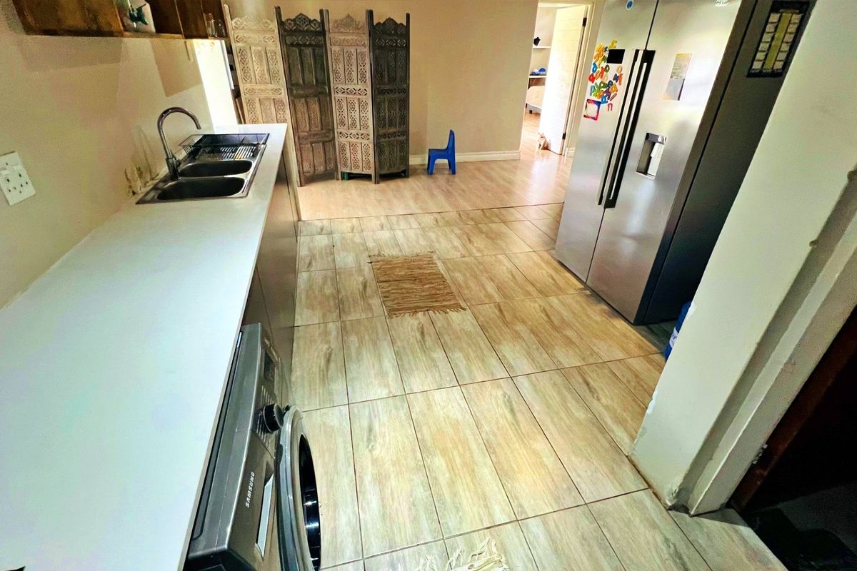 A functional kitchen and laundry area featuring tiled flooring, a double sink, and built-in cabinetry with space for integrated appliances.