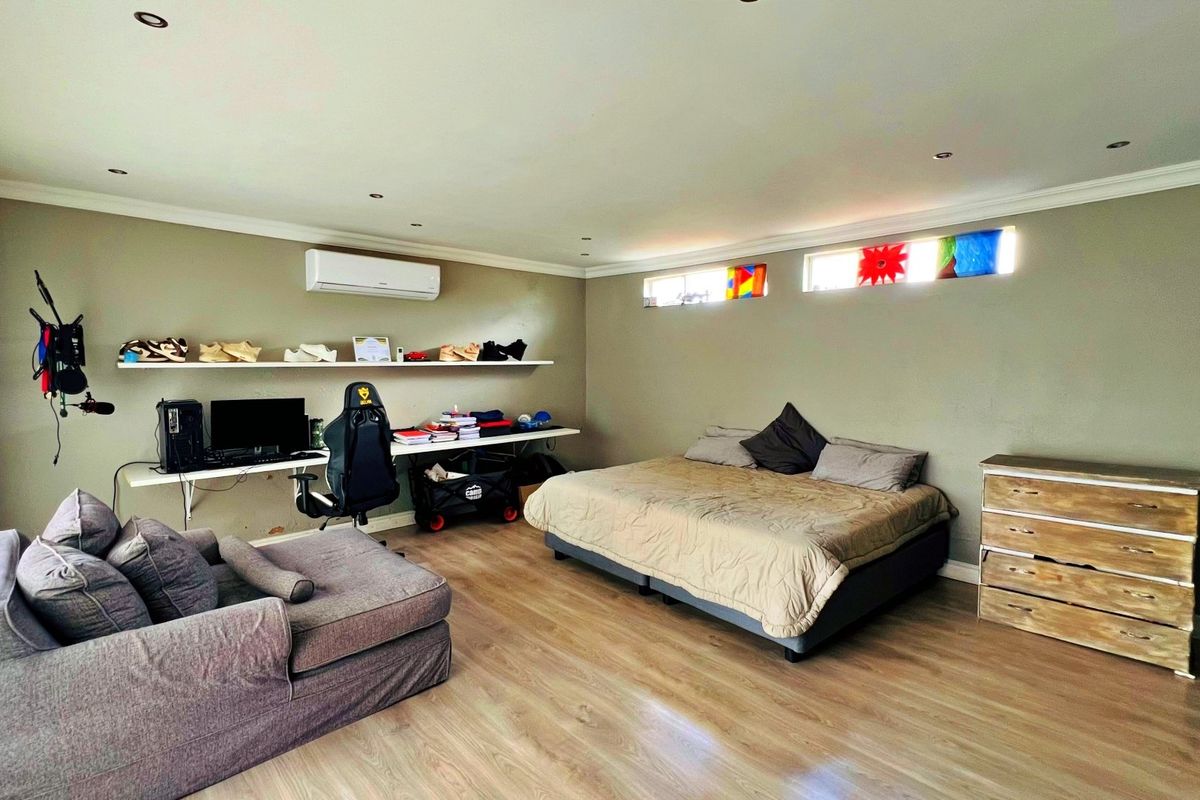 Spacious bedroom featuring light wood-look flooring, wall-mounted air conditioning unit, built-in shelving, and high-level clerestory windows.