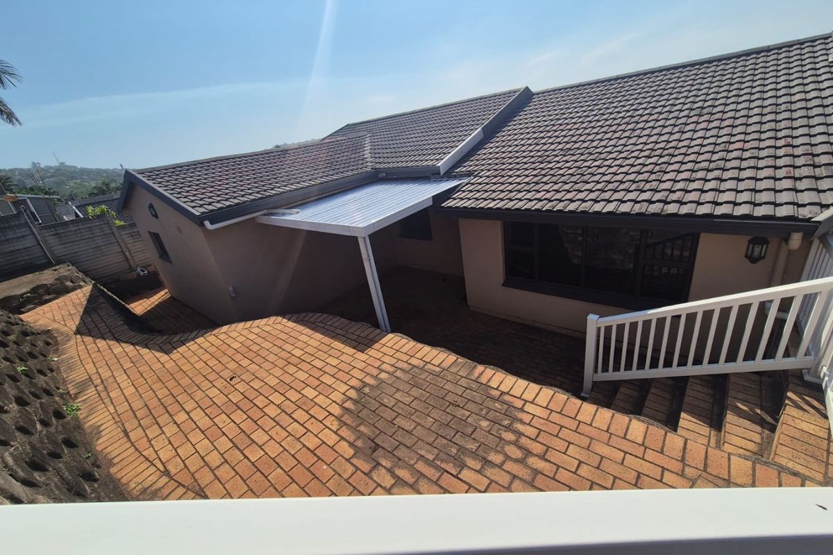 Rear exterior view of the property featuring a tiled roof, brick paved patio area, and a covered outdoor space with retaining wall.