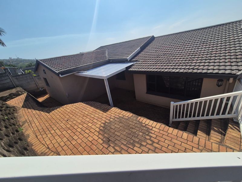 Rear exterior view of the property featuring a tiled roof, brick paved patio area, and a covered outdoor space with retaining wall.