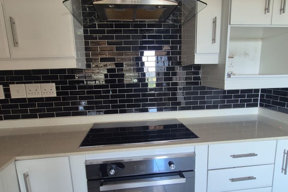 Modern kitchen featuring glossy white cabinetry, contrasting black subway tile backsplash, quartz countertops, and integrated stainless steel appliances including an oven and extractor fan.