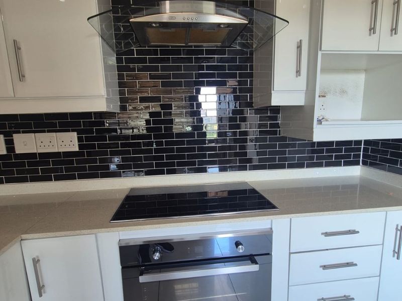 Modern kitchen featuring glossy white cabinetry, contrasting black subway tile backsplash, quartz countertops, and integrated stainless steel appliances including an oven and extractor fan.