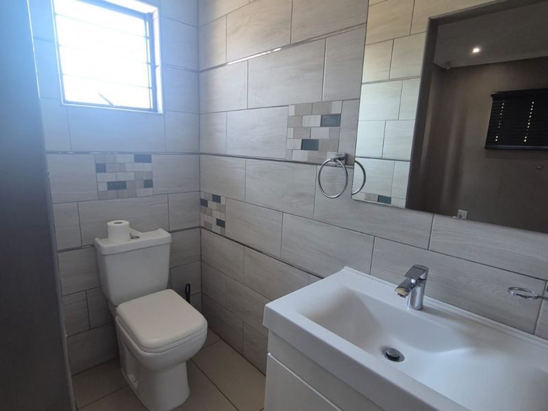 Modern bathroom featuring a vanity cabinet with basin, wall-mounted mirror, and neutral tiled finishes throughout.
