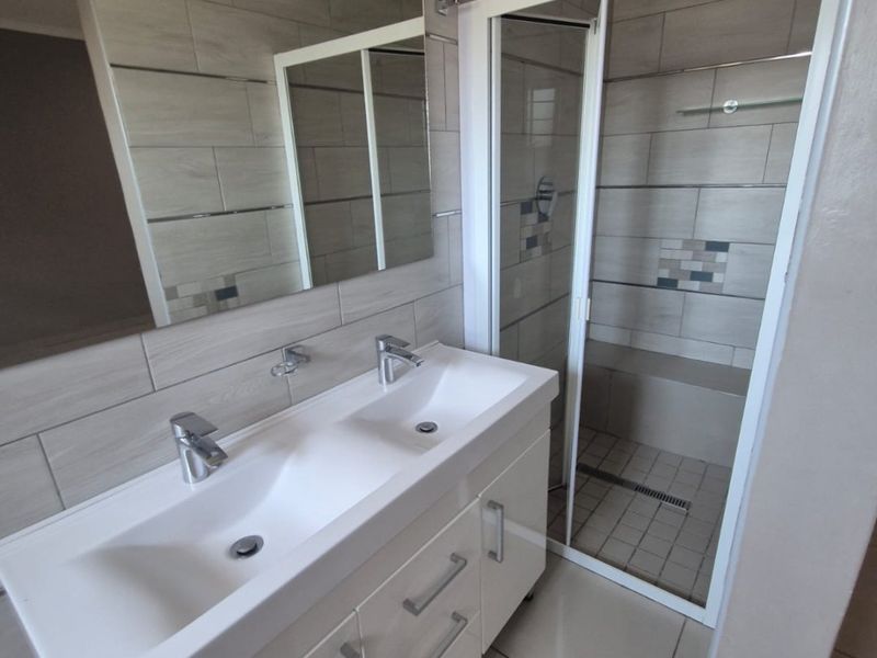 Modern bathroom featuring a double vanity with white cabinetry, large wall-mounted mirror, and a walk-in shower with a built-in bench and rain shower head.