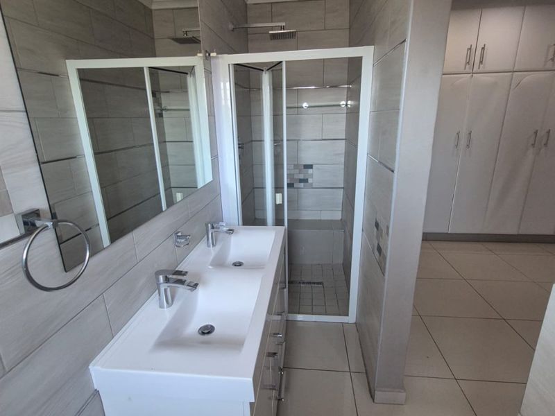 Modern bathroom featuring a double vanity, walk-in shower with glass enclosure, and ample built-in storage cupboards with neutral tiled finishes.