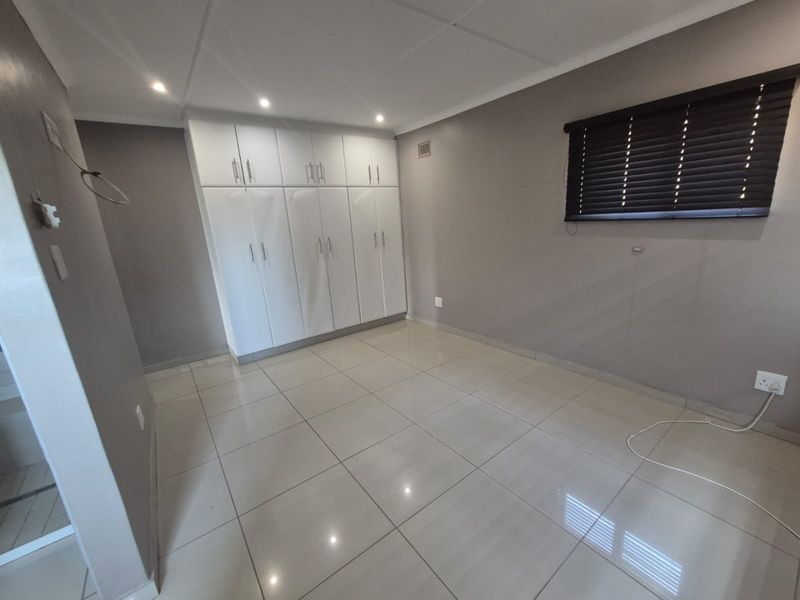 A clean, empty bedroom featuring neutral grey walls, large white built-in cupboards, tiled flooring, and recessed downlighting.