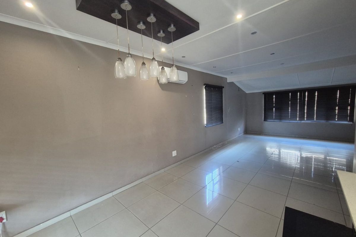 Spacious, empty living area featuring large format floor tiles, modern pendant lighting, and a wall-mounted air conditioning unit.