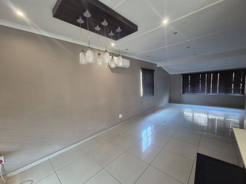 Spacious, empty living area featuring large format floor tiles, modern pendant lighting, and a wall-mounted air conditioning unit.