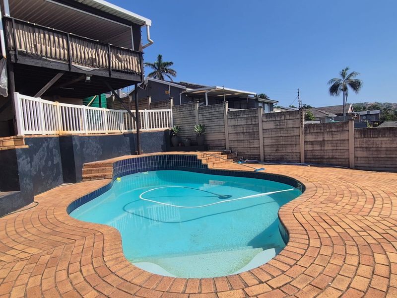 Outdoor pool area featuring a curved swimming pool, brick paved surround, and a raised wooden deck attached to the main house structure.