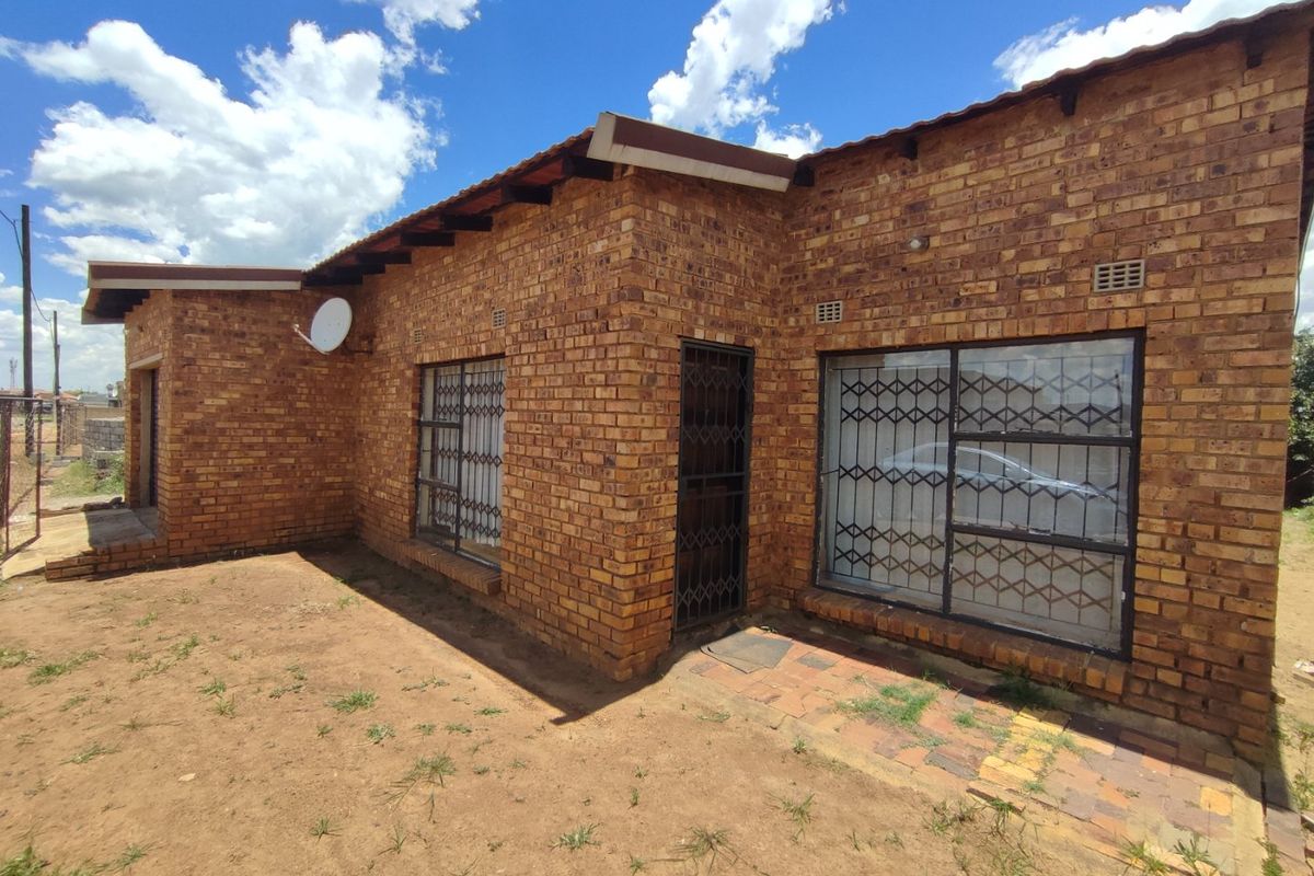 Rear view of a face-brick house featuring security gates and bars on windows, set on a plot with natural ground.