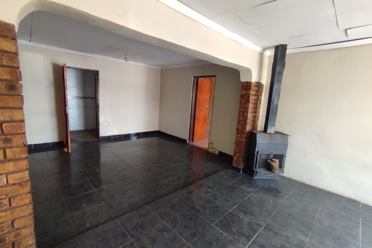 An empty living room featuring dark tiled flooring, an exposed brick pillar, and a freestanding fireplace, offering a blank canvas for renovation.