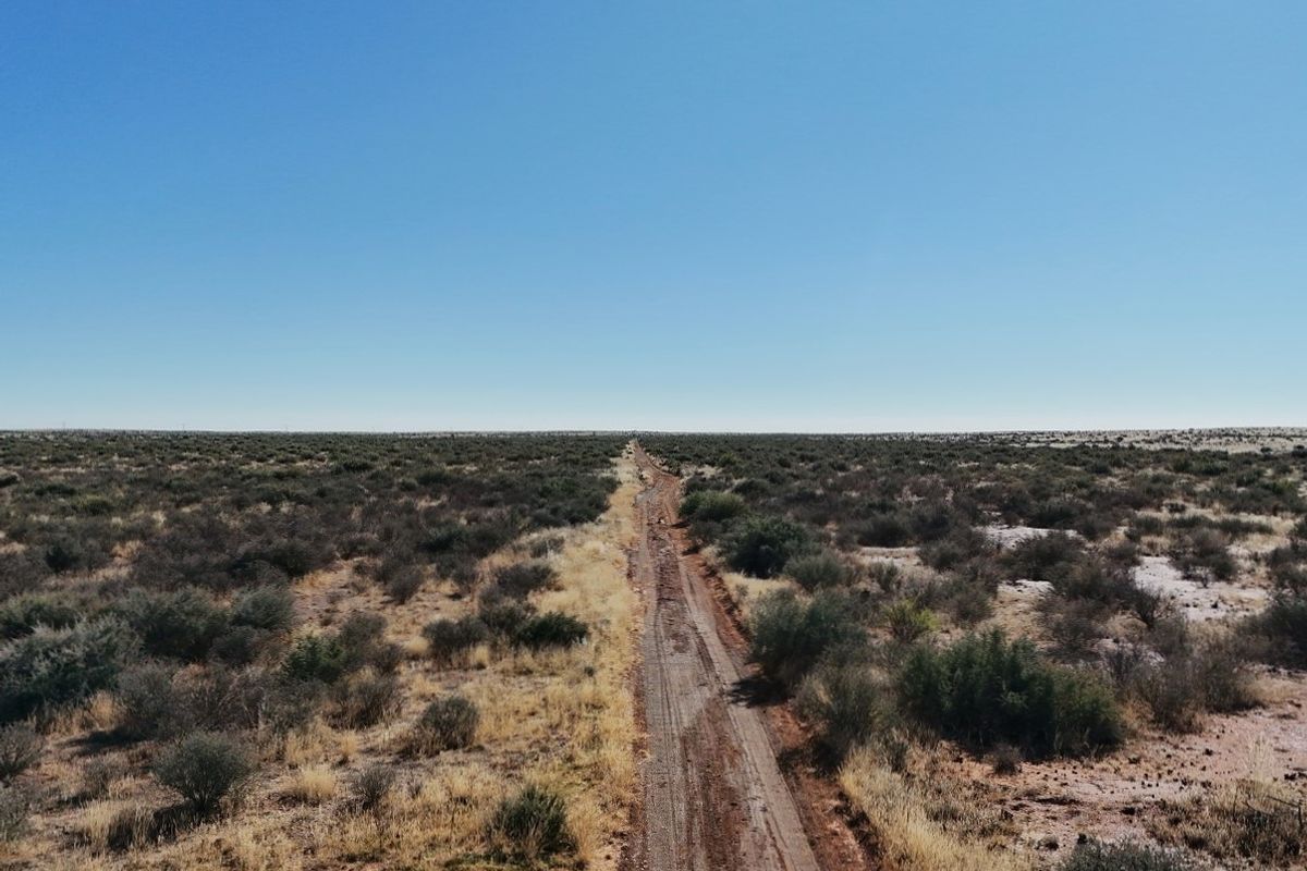 An aerial view of a long dirt access road stretching through the expansive, arid landscape of the farm property.