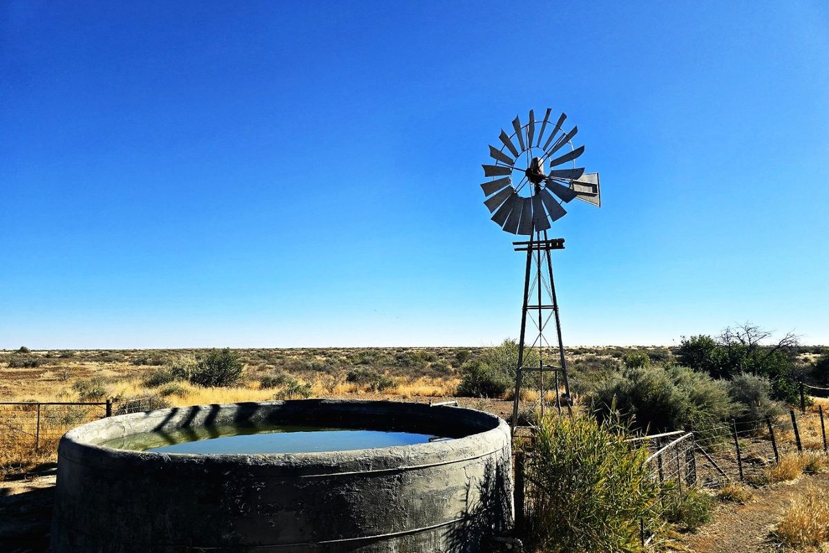 A traditional farm windmill positioned next to a concrete water reservoir in an open, arid landscape.