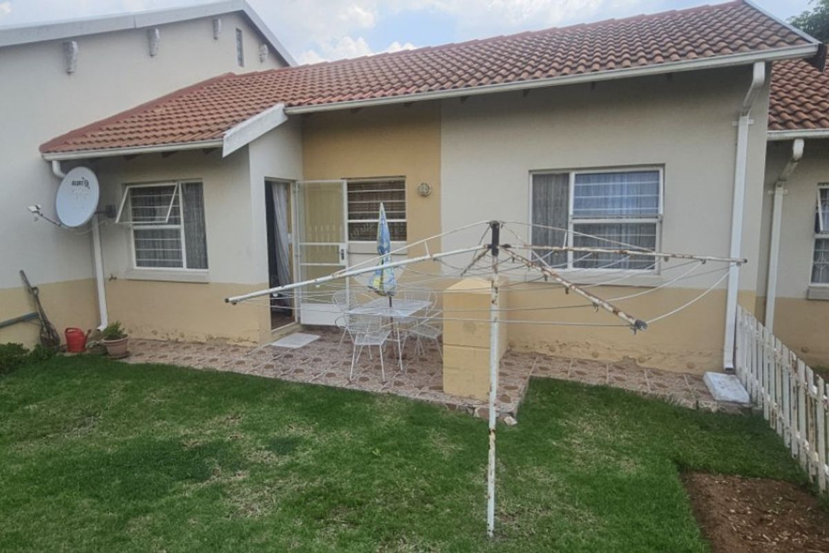 Rear view of the apartment featuring a small tiled patio, security gates, and a private garden area with a picket fence.