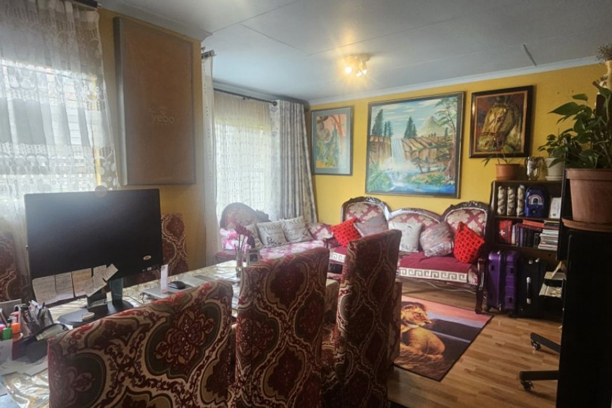 A living room area featuring laminate flooring and ceiling cornicing, currently utilized as a multi-purpose living and workspace.
