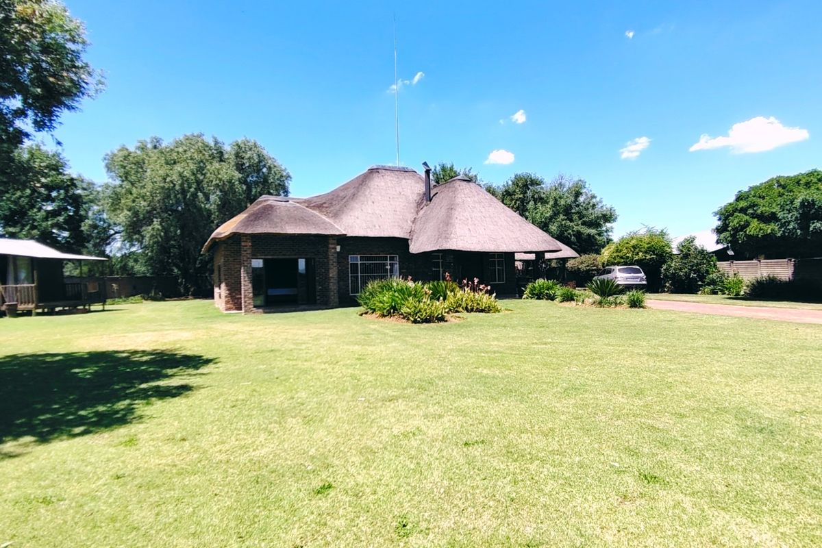 A rear view of a traditional farmhouse featuring a classic thatch roof, brick exterior, and expansive surrounding garden space.