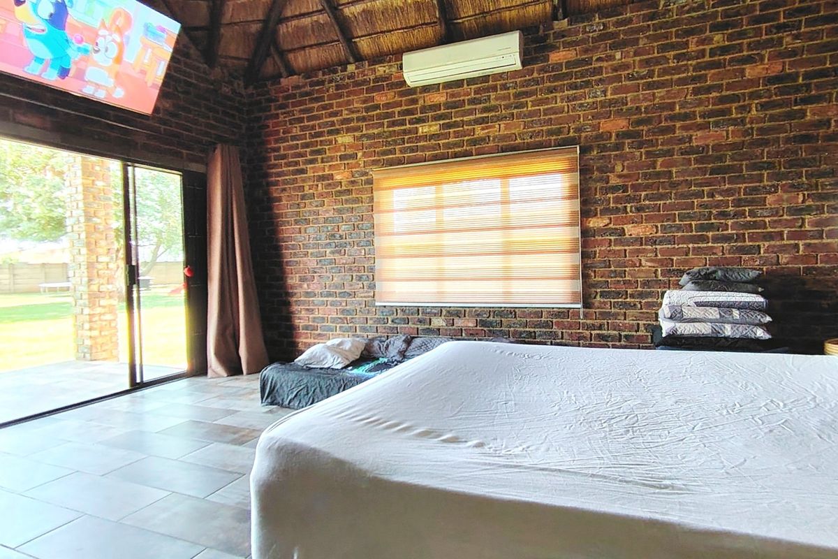 Spacious bedroom featuring exposed brick walls, a high thatched ceiling, tiled floors, and large sliding glass doors providing direct access to the garden.